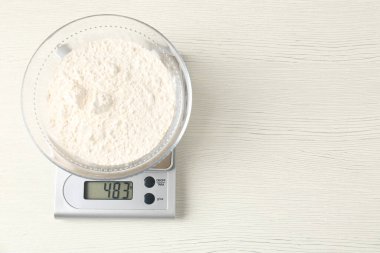 Elektronik mutfak terazisi, beyaz ahşap masa üzerinde bir kase un, üst manzara. Metin için boşluk