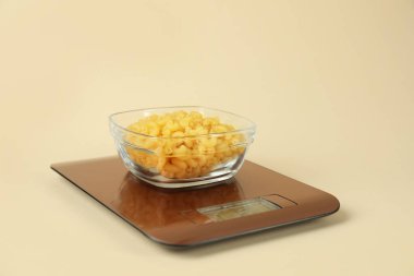 Bej arka planda bir kase çiğ makarna ile elektronik mutfak terazisi, yakın plan.