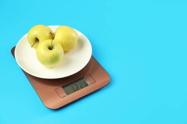 Elektronik mutfak terazisi ve açık mavi arka planda elmalar. Metin için boşluk
