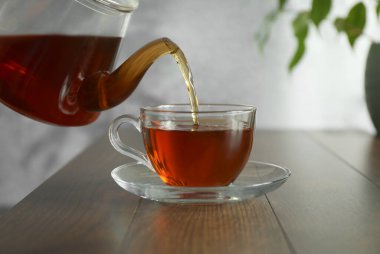 Tahta masada çaydanlıktan fincana taze demlenmiş çay dökülüyor, yakın plan.