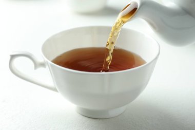 Beyaz masada çaydanlıktan fincana taze demlenmiş çay dökülüyor, yakın plan.