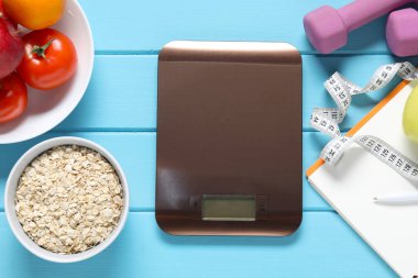 Elektronik mutfak terazisi, mezura, halterler ve ürünler açık mavi ahşap masa üzerinde düz konum. Diyet