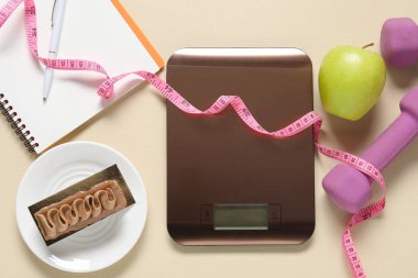 Elektronik mutfak terazisi, mezuralar, dambıllar, not defterleri ve bej masadaki ürünler, düz yatak. Kalori kontrolü