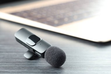 Lavalier mikrofon ve laptop siyah ahşap masada, yakın plan.