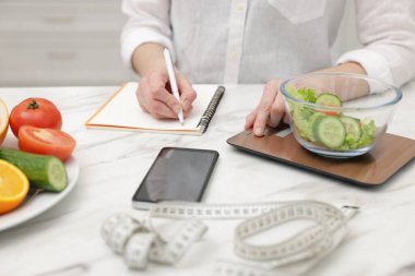 Salata tartan ve beyaz masadaki deftere yazan kadın, yakın plan.