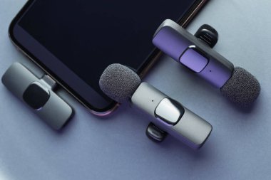 Lavalier mikrofonlar ve açık gri arka planda akıllı telefon, düz konum