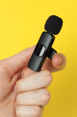 Sarı arka planda lavalier mikrofon tutan kadın, yakın plan.
