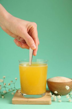 Turkuaz arka planda suda kolajen tozu karıştıran kadın, yakın plan.