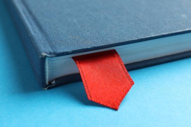 Açık mavi arkaplanda kırmızı kurdele yer imi olan kitap, yakın plan