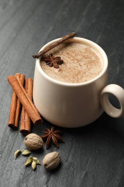 Fincanda Aromatik Masala çayı ve siyah masada baharatlar, yakın plan.