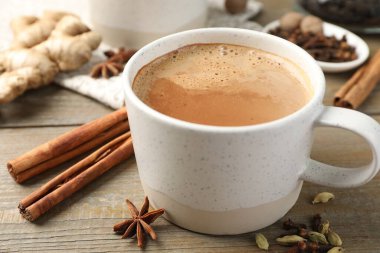 Aromatik Masala çayı fincanda ve baharatlar ahşap masada, yakın plan.