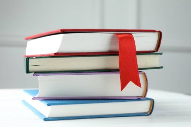 Kırmızı kurdele yer imi ve beyaz ahşap masada gri duvara dayalı renkli kitap, yakın plan.