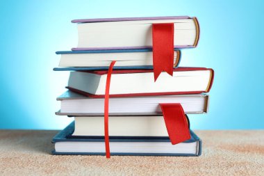 Açık mavi arkaplana karşı desenli tabloda kırmızı kurdele yer imlerine sahip kitaplar, yakın plan