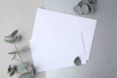 Boş tebrik kartı, kağıt zarf ve okaliptüs yaprakları açık gri arka planda, düz yatıyordu.