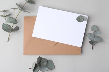 Boş tebrik kartı, kağıt zarf ve okaliptüs yaprakları açık gri arka planda, düz yatıyordu.