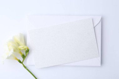 Boş tebrik kartı, beyaz arka planda kağıt zarf ve çiçek, düz uzanmış.