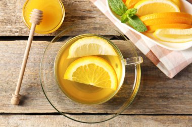 Cam fincanda aromatik meyve çayı, portakal, limon, bal ve nane, ahşap masada düz uzanmış.