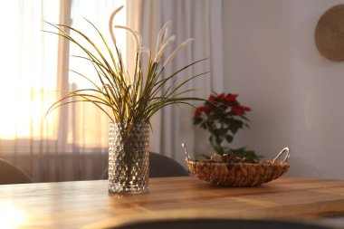 Pencerenin yanındaki ahşap masadaki vazoda perdeler var.