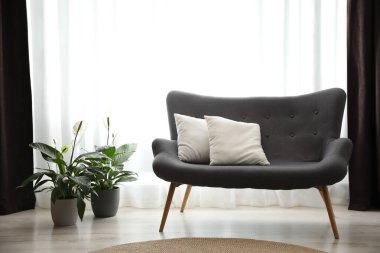 Pencerenin yanında rahat bir kanepe, odada zarif perdeler var.