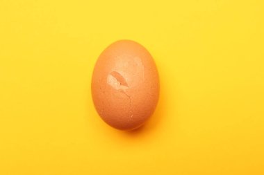 Sarı arka planda kırık kabuklu bir yumurta, üst manzara.
