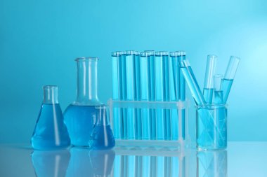 Aynanın yüzeyinde mavi arkaplana karşı sıvı bulunan laboratuvar camları.