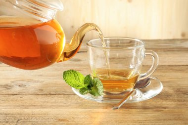 Çaydanlıktan cam fincana taze demlenmiş çay dökülüyor ahşap masada, yakın plan.