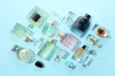 Bottles of various perfumes on light blue background, flat lay