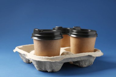 Kağıt kahve bardakları mavi arka planda karton tutacakta, yakın plan.