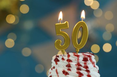 50. yaş günü. Kek üzerindeki mumların yanma sayısı bulanık arka planda ışıklarla, yakın planda. Bokeh etkisi
