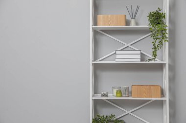 Açık gri duvarın yanındaki raflarda farklı eşyalar var. Metin için boşluk