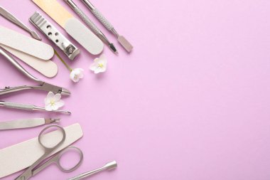 Pembe arka planda farklı manikür aletleri ve çiçekler var. Metin için boşluk