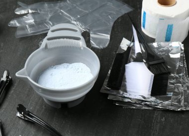 Beyazlatma tozu ve kuaför aletleri siyah masada, yakın plan.