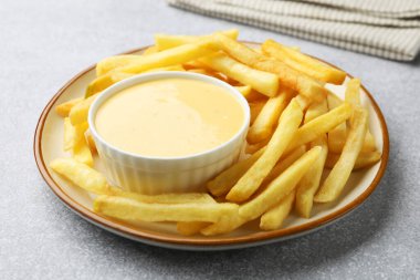 Lezzetli peynir sosu kasede ve patates kızartması gri masada, yakın plan.