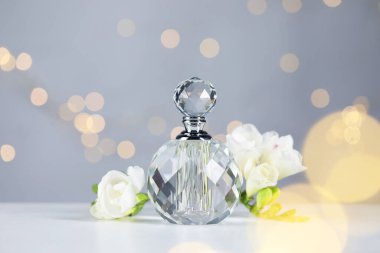 Bir şişe aromatik parfüm ve çiçek, arka plandaki gri ışıklara karşı, yakın plan. Bokeh etkisi