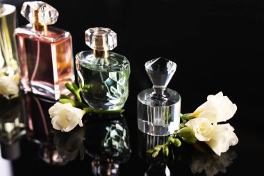 Siyah ayna yüzeyinde aromatik parfüm şişeleri ve çiçekler, yakın plan.