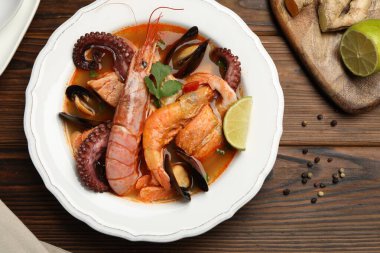 Lezzetli deniz ürünleri çorbası kasede, kireç ve baharatlar ahşap masada, düz yerde.