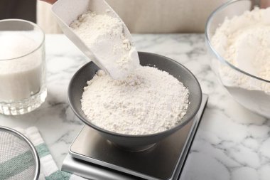 Beyaz mermer masadaki dijital mutfak terazisine şeker koyan kadın, yakın plan.