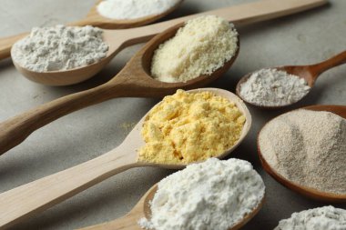 Açık gri masada kaşıklarda farklı türde un, yakın plan.