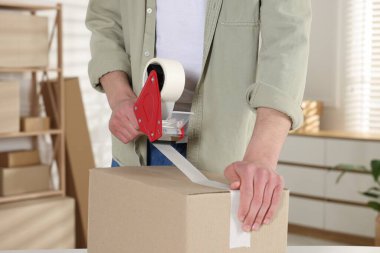 Karton kutuyu kapalı bir yere kapatmak için yapıştırıcılı bant kullanan bir adam.