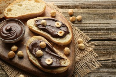 Çikolata sürülmüş ekmek dilimleri ve ahşap masanın üzerinde fındıklar.