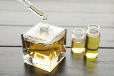 Siyah ahşap arka planda damlatan parfüm şişesinden aromatik yağ almak, yakın plan.