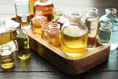 Siyah ahşap arka planda aromatik yağlı parfüm şişeleri, yakın plan.