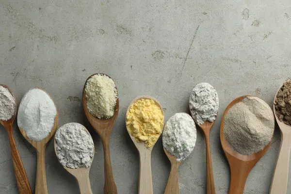 Açık gri masadaki kaşıklarda farklı türde un, düz. Metin için boşluk