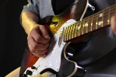 Siyah arkaplanda arabulucuyla gitar çalan adam, yakın plan