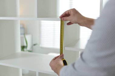 Beyaz rafları bantla ölçen adam içeride, yakın plan.