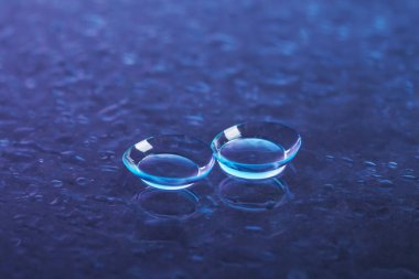Mavi ayna yüzeyine bir çift kontakt lens ve su damlası, yakın plan.