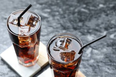 Kola buz küpleriyle tazeleniyor ve koyu dokulu masa üzerinde pipetler, yakın plan.