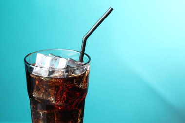 Kola, buz küpleriyle tazeleniyor ve turkuaz eğimli arka planda bardakta pipet bulunuyor. Yakın plan. Metin için boşluk