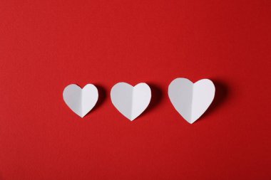 Kırmızı zemin üzerinde beyaz kağıt kalpler, düz uzanmış