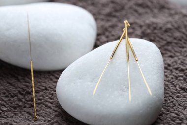 Akupunktur iğneleri ve spa taşları kahverengi havluda, yakın plan.